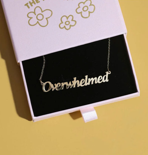 Gold "Overwhelmed" nameplate necklace in a purple slide-open box with black felt lining rests on a yellow surface