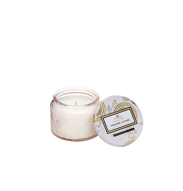 White embossed glass Panjore Lychee Voluspa candle jar with metallic floral lid set to the side