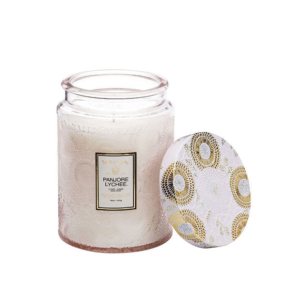 Whitish embossed glass Panjore Lychee Voluspa jar candle with metallic white and gold lid removed and set to the side