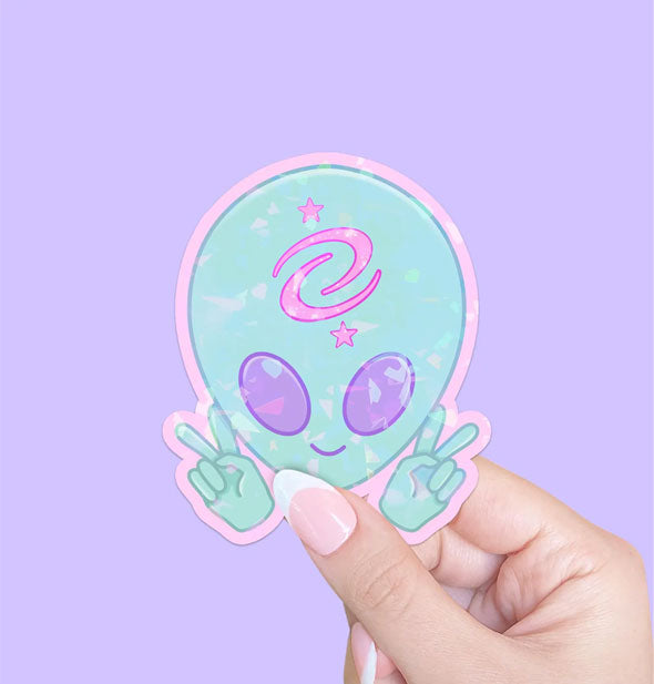 Model's hand holds a peace sign-flashing blue alien sticker with purple eyes and a pink symbol on its forehead