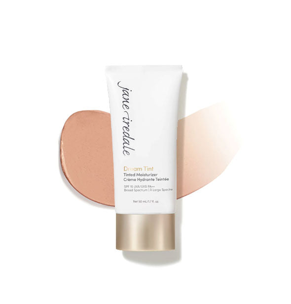 White and gold tube of Jane Iredale Dream Tint Tinted Moisturizer with enlarged smeared product application behind in shade Peach Brightener