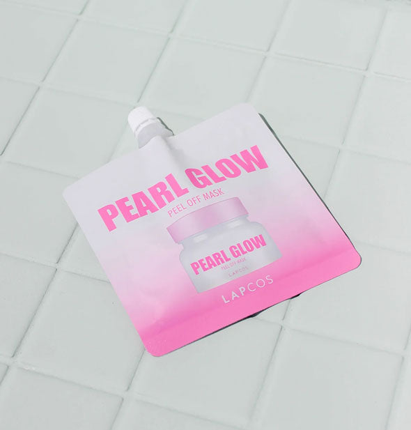 Pink and white pack of Lapcos Pearl Glow Peal Off Mask rests on a white tiled surface