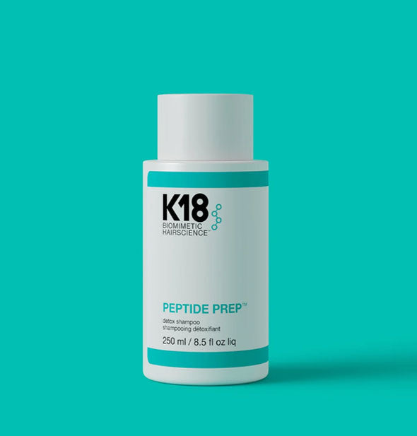 White 8.5 ounce bottle of K18 Biomimetic Hairscience Peptide Prep Detox Shampoo on a teal background