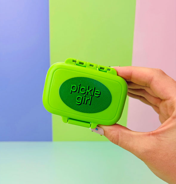 Model's hand holds a bright green pill case with dark green oval that says, "Pickle Girl" inside it in shadow-effect lettering