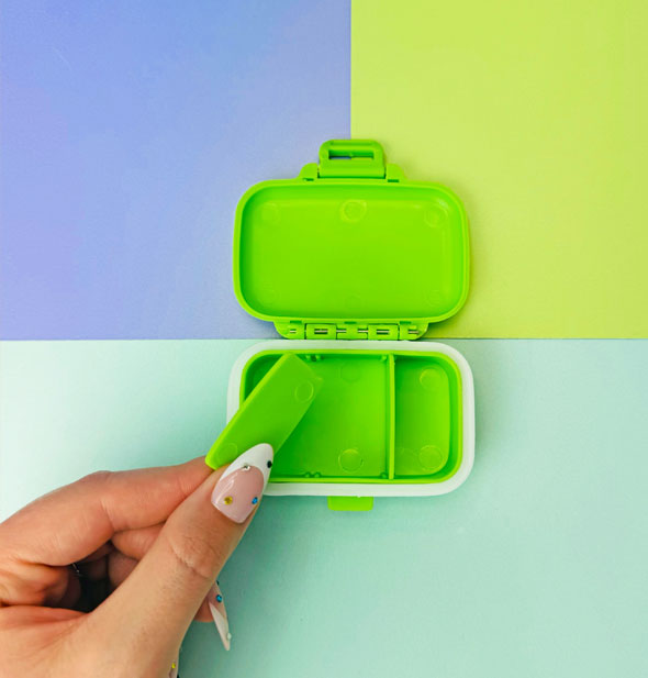 Model removes an interior divider from a bright green pill case to create two compartments