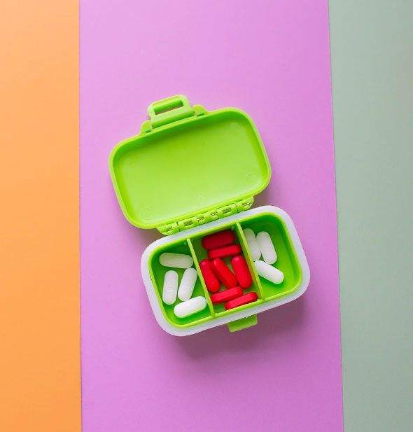 Opened green pill case with three compartments holds white and red tablets