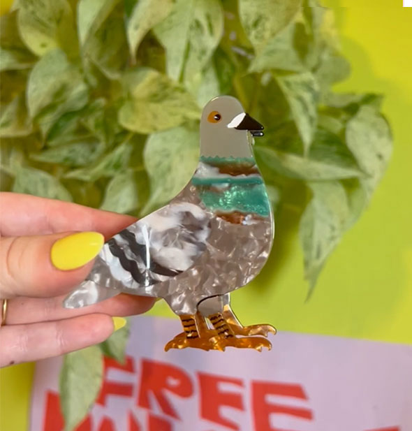 Model's hand holds a hair clip designed to resemble a pigeon