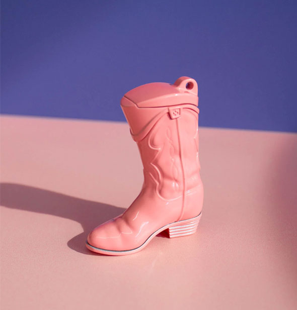 Pink cowgirl boot lighter on a pink surface against a purple backdrop