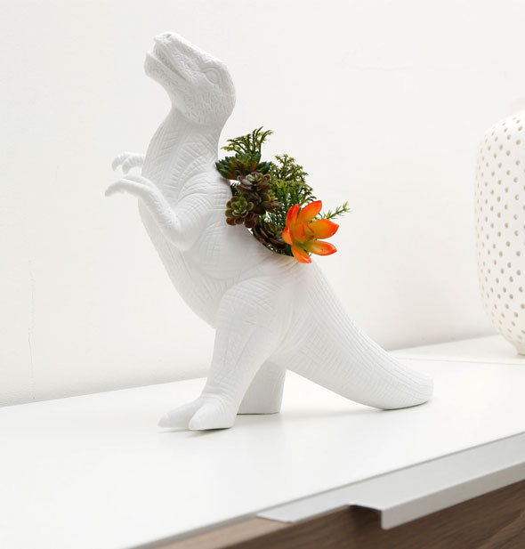 White ceramic Tyrannosaurus rex vase on an office cabinet holds a small arrangement of flowers and succulents