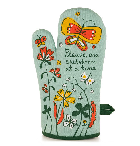 Pale green oven mitt with dark green bottom piping and hanging loop says, "Please, one shitstorm at a time" in script surrounded by colorful floral and butterfly graphics