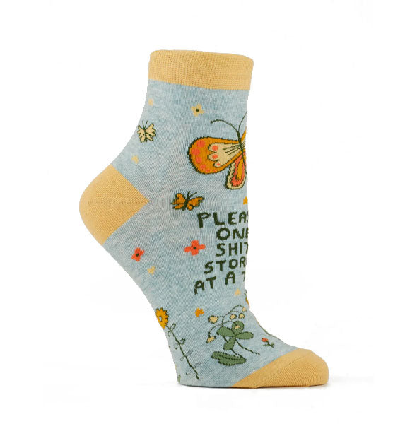 Gray ankle sock with yellow accents and colorful floral and butterfly designs say, "Please, one shit storm at a time"