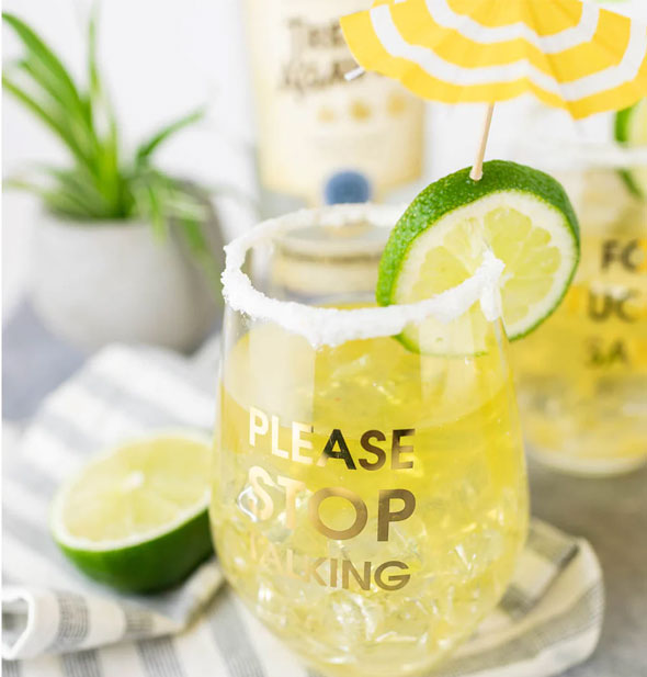Please Stop Talking stemless wine glass is filled with a beverage and garnished with a lime slice toothpicked with a yellow and white umbrella