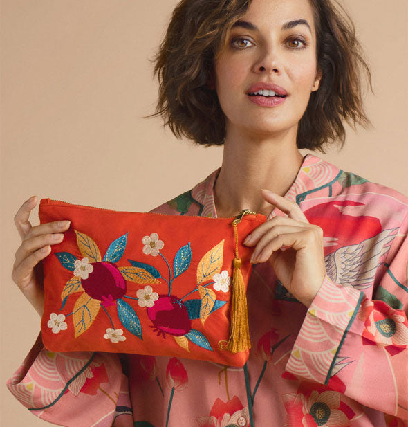 Model poses with an orange velvet zippered pouch featuring colorful embroidered pomegranates, leaves, and flowers design