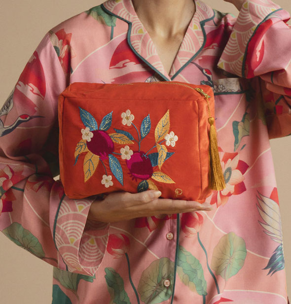 Model holds a red-orange Luxury Velvet Wash Bag with pomegranate design