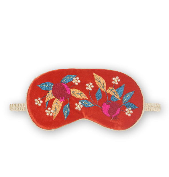 Red-orange sleep mask with taupe piping and elastic band features colorful embroidered artwork on teal and gold leaves with small white flowers and purple pomegranates