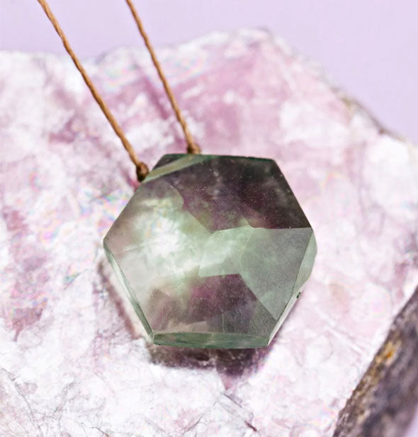 Faceted greenish hexagonal gemstone necklace on gold corn rests on a piece of purple quartz