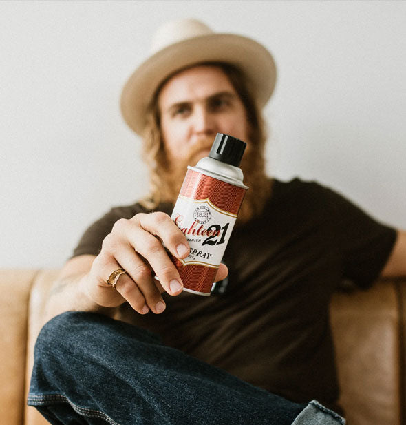 Model sitting back on a sofa holds a can of hairspray forward to camera