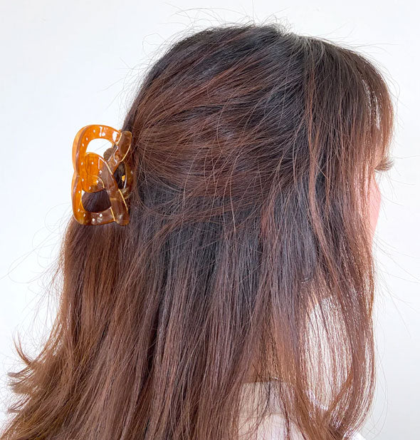 Model wears a pretzel clip in a partially swept-back hairstyle