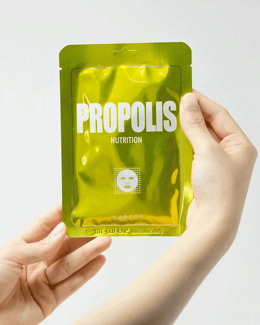 Model removes a Propolis Nutrition Sheet Mask from metallic yellow packet and unfolds it