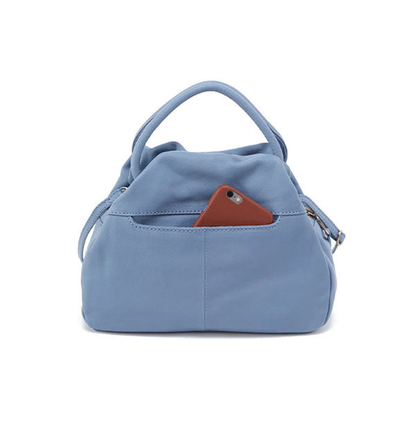 Reverse side of pale blue leather satchel bag reveals an exterior slip pocket out of which a phone is partially emerging