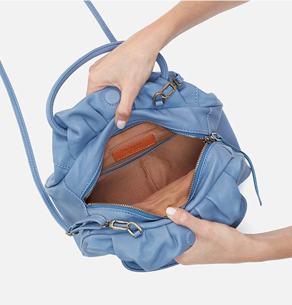 Model's hands hold open a pale blue leather satchel bag to reveal its tan interior