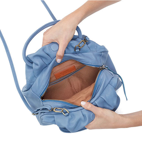 Model's hands hold open a pale blue leather satchel bag to reveal its tan interior