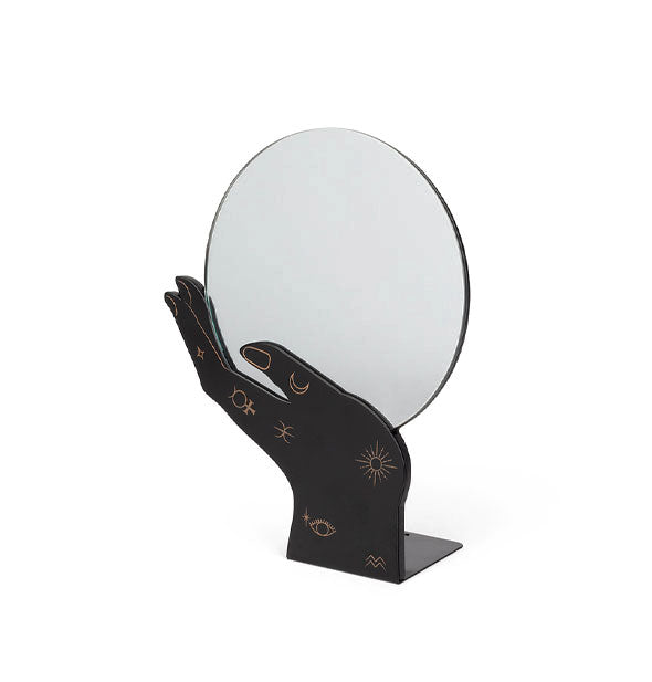 A black hand with gold fingernail detail and mysterious symbols holds a round mirror