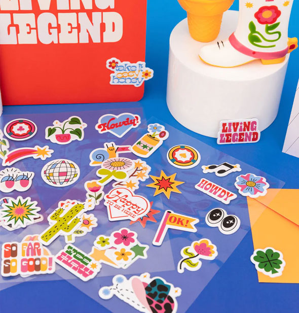 Transparent sheets of colorful stickers are staged on a blue backdrop with other items