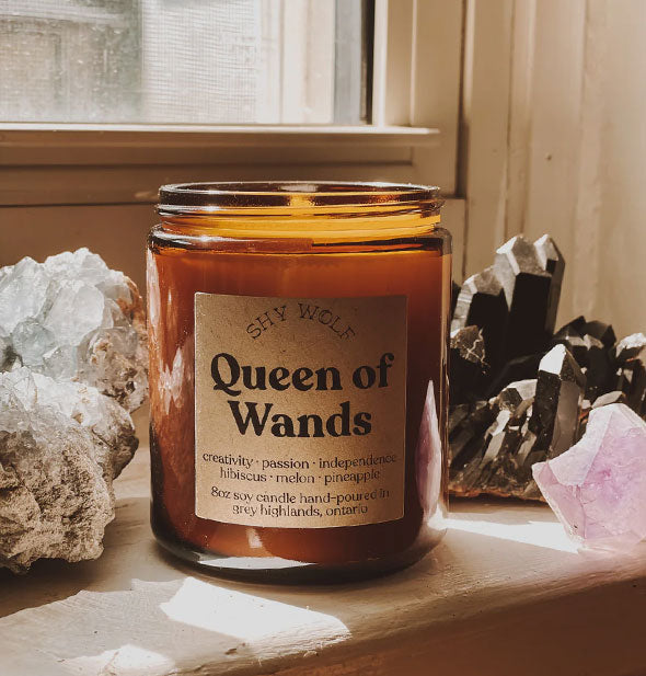 Lit Queen of Wands Shy Wolf candle on windowsill with crystals