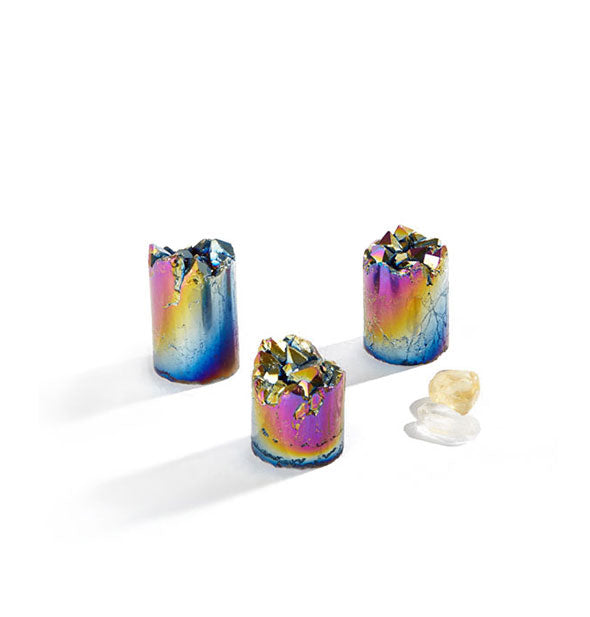 Three cylindrical iridescent rainbow quartz pieces with raw tops, and two pieces of lighter-colored quartz alongside