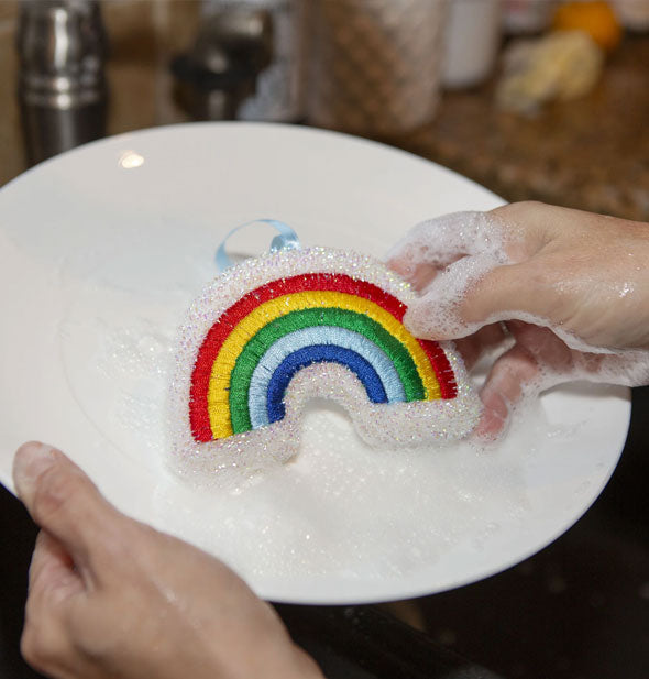 Model demonstrates use of a Rainbow Scrub Sponge on a sudsy white dinner plate