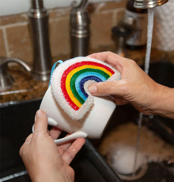 Model demonstrates use of a Rainbow Scrub Sponge on a white coffee mug over a sink basin