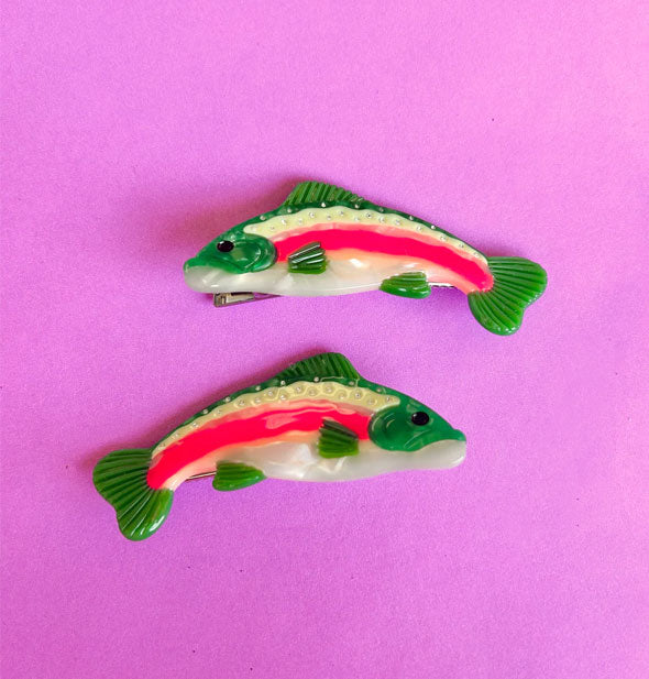 Pair of green, white, and pink rainbow trout hair clips rest on a purple surface