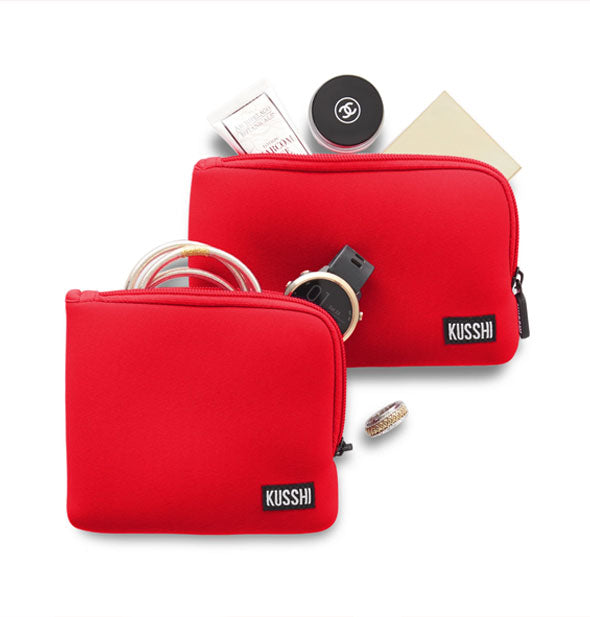 Two bright red KUSSHI pouches, one square and one rectangular, with personal items appearing to fall out of each