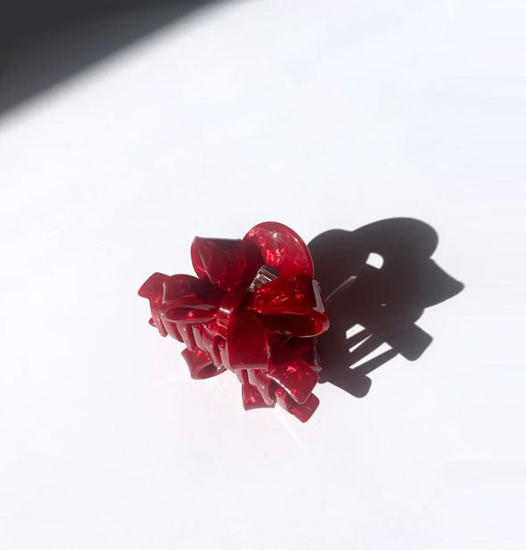 Red quartz-effect ribbon bow claw clip casts a long shadow on a light surface