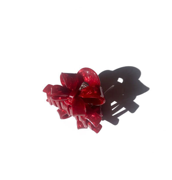 Red quartz-effect ribbon bow claw clip casts a long shadow on a light surface