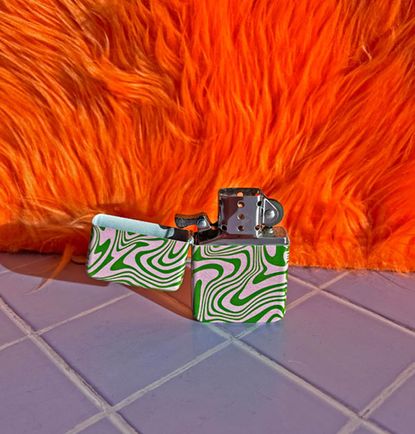 Opened pink and green psychedelic swirl print refillable lighter on a purple tile surface against an orange fur backdrop