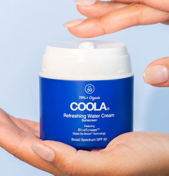 Model dips finger into an opened pot of Coola Refreshing Water Cream Sunscreen