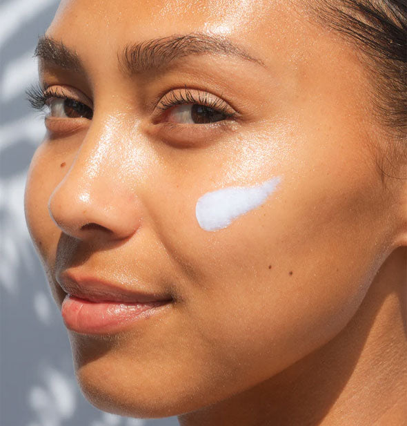 Model has a thick, unblended application of Coola Refreshing Water Cream Sunscreen on cheek