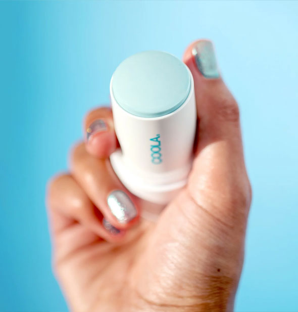 Model's hand holds an open tube of Coola Refreshing Water Hydration Stick Sunscreen