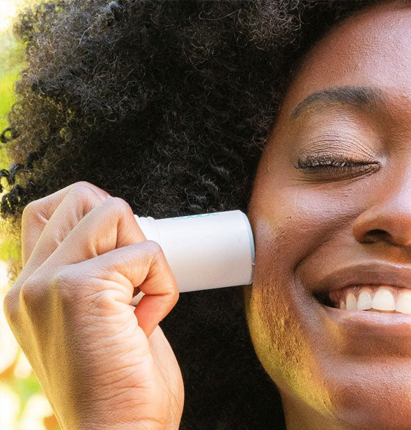 Smiling model applies Coola Organic Refreshing Water Hydration Stick Sunscreen to cheek