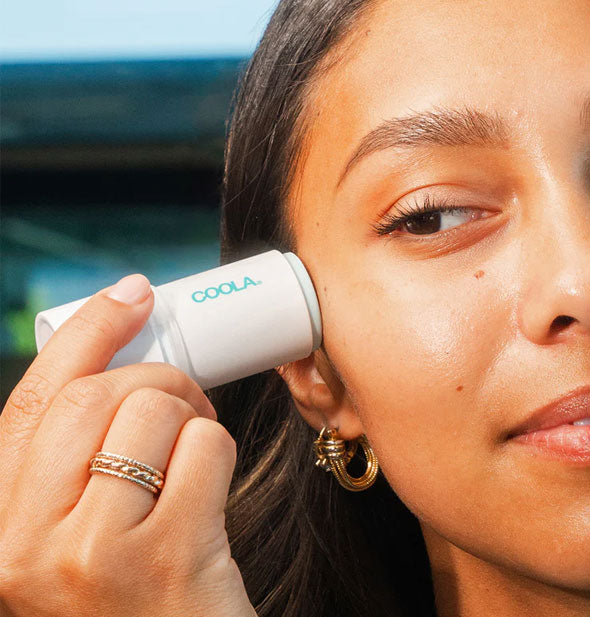 Model applies Coola Refreshing Water Hydration Stick Sunscreen to cheek