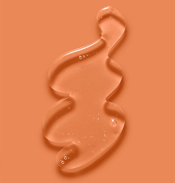 Clear, slightly bubbly squiggle of Verb Reset Clarifying Shampoo on an orange surface