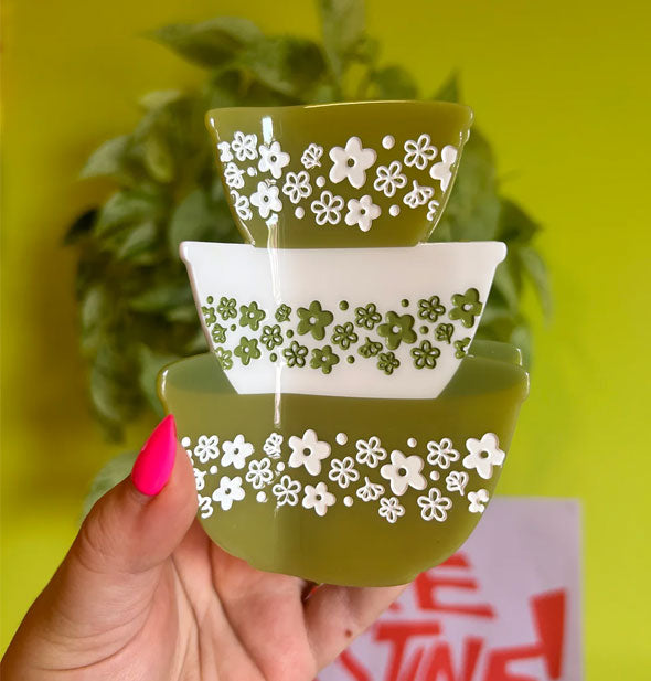 Model's hand holds a hair clip designed to resemble a stack of three green and white retro Pyrex bowls with daisy print