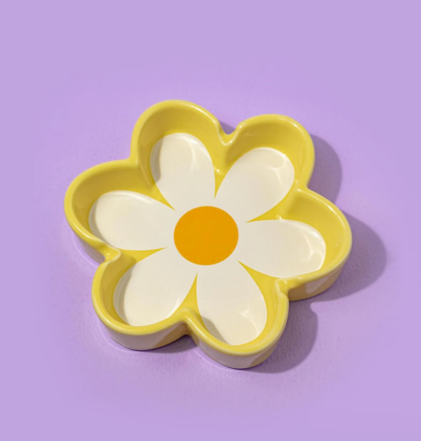 Yellow ashtray with white and orange daisy design in the bottom rests on a purple backdrop
