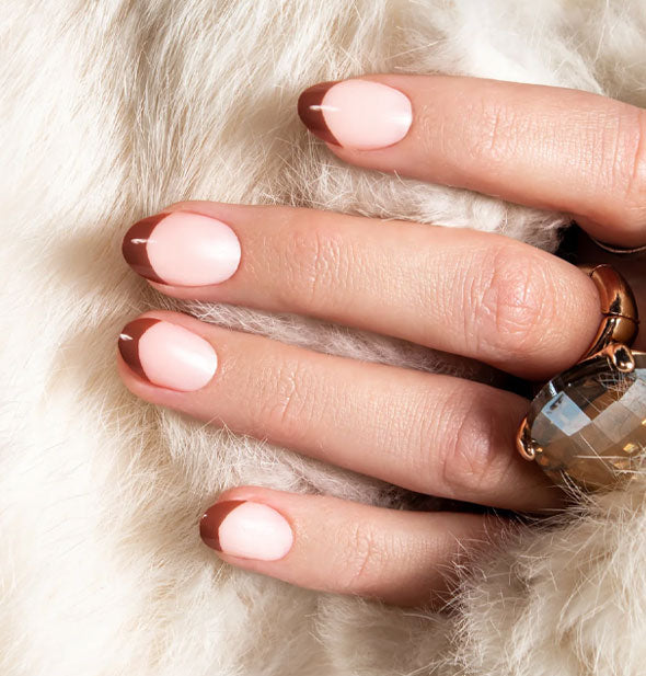 Model's hand wears a set of French manicure style press-on nails with a white base and brown tip