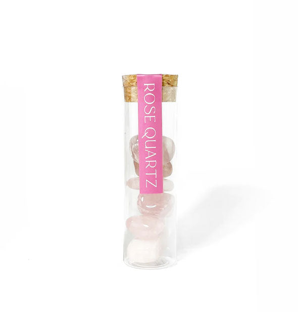 A clear vial filled with six rose quartz stones is topped with a cork lid and pink label with white lettering