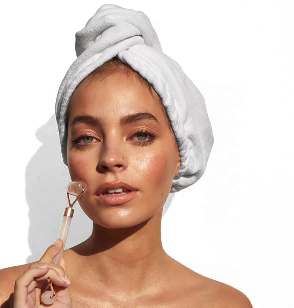 Model wearing hair towel demonstrates use of a gemstone facial roller on cheek