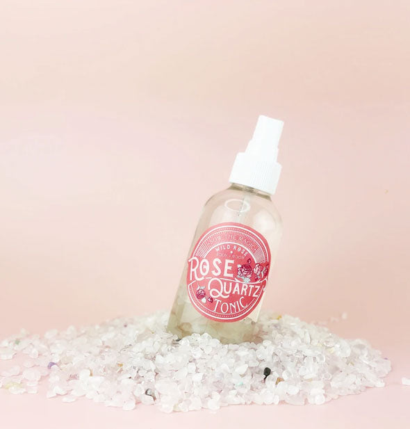 Bottle of Rose Quartz Tonic spray positioned on a tilt on a mound of small white gemstones