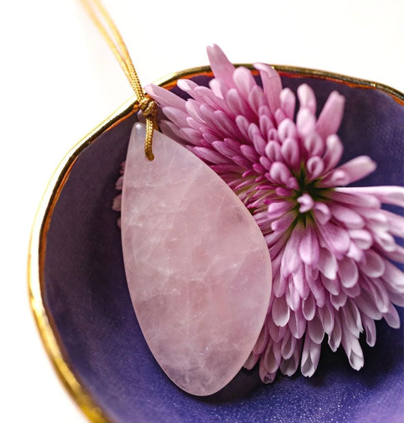 Rose quartz stone necklace on gold cord rests in a purple and gold dish with a pink chrysanthemum